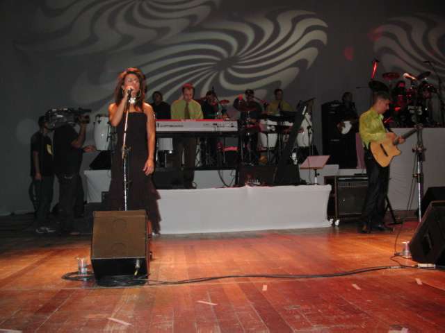 Visão ampla do palco com vocalista e banda em segundo plano
