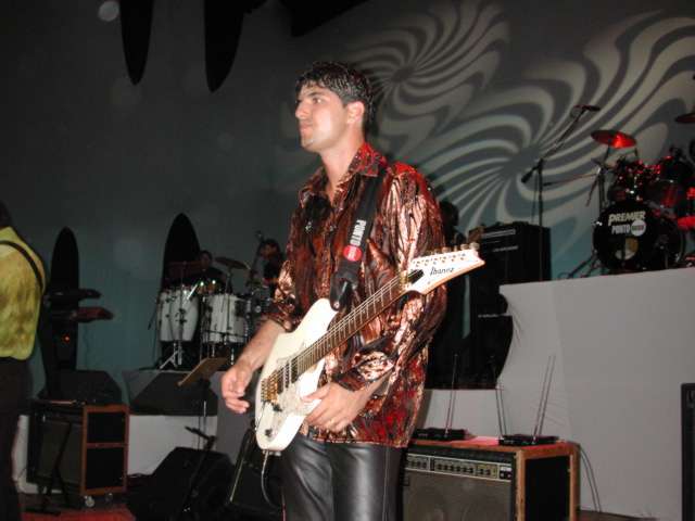 Guitarrista com camisa estampada e guitarra Ibanez branca no palco