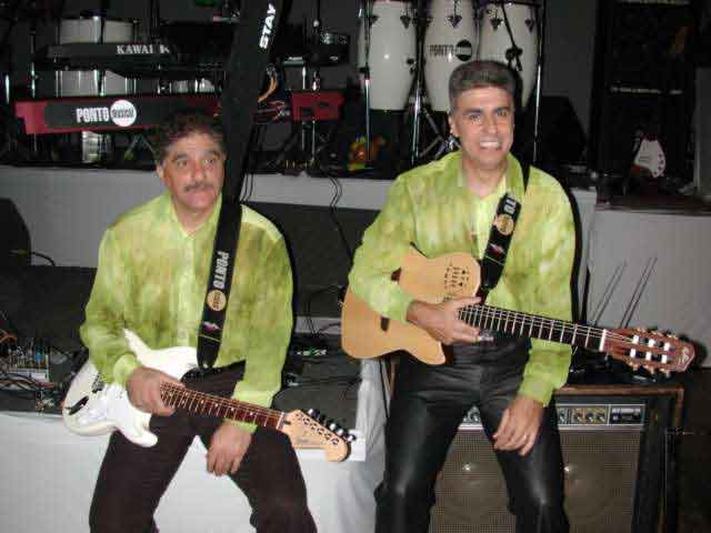 Dupla de músicos com guitarras e violão sentados no palco
