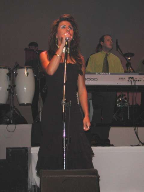 Cantora em vestido preto cantando no pedestal do microfone