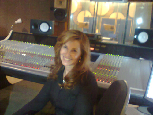 Produtora sorrindo no centro da sala de mixagem