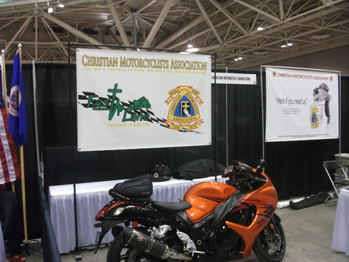 Estande do Christian Motorcyclists Association com motocicleta laranja